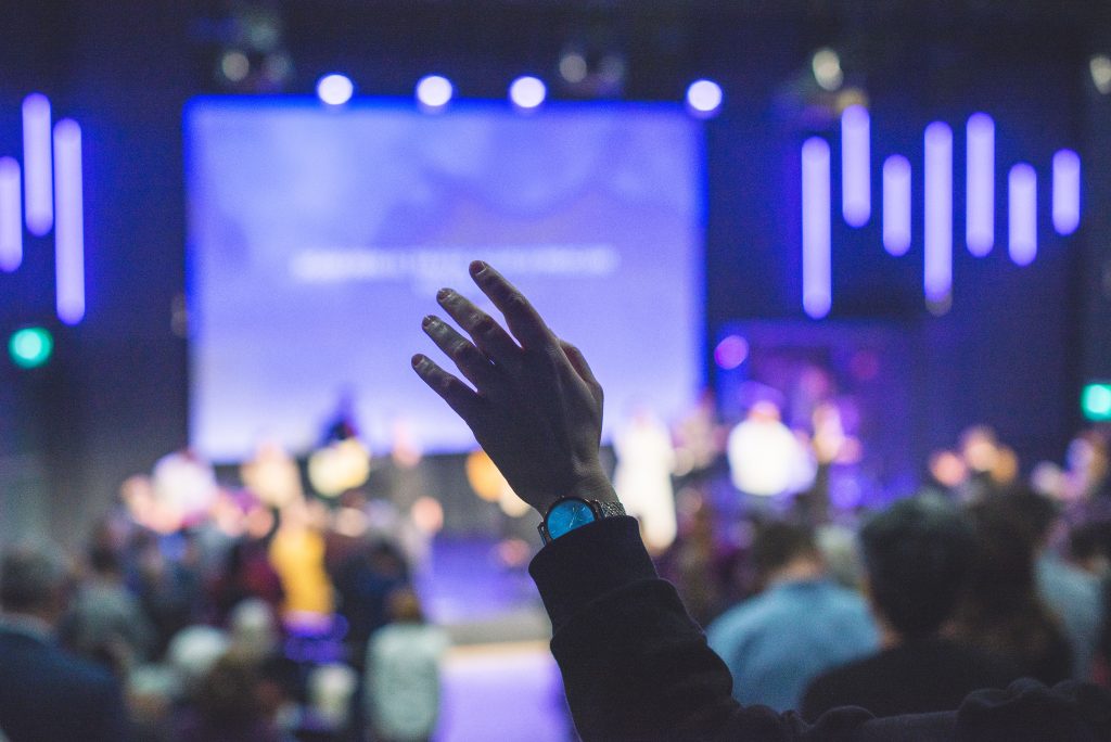 Church attendees raising their hands in worship in front of a large screen: Graphic Design for Churches: Why it matters and how to do it well